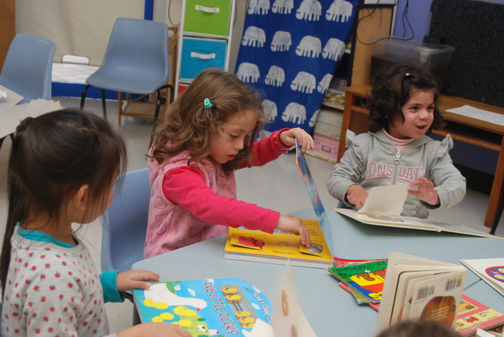 Preschool girls sitting at a table reading picture books